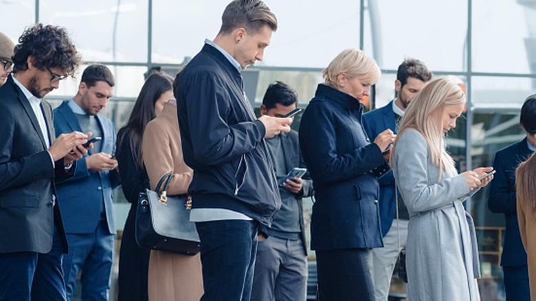 Un groupe de personnes en public regardant toutes leur smartphone