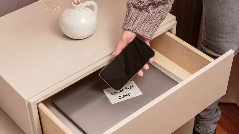 Une femme plaçant un smartphone dans un tiroir avec une note à l'intérieur qui dit : 