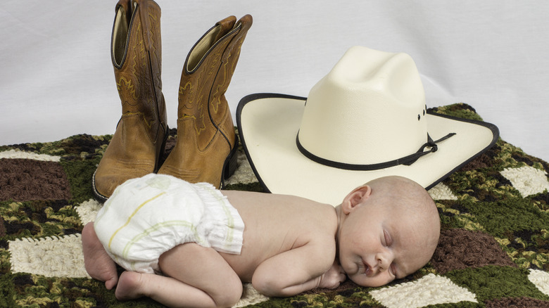 Un bébé posé avec des bottes de cowboy et un chapeau