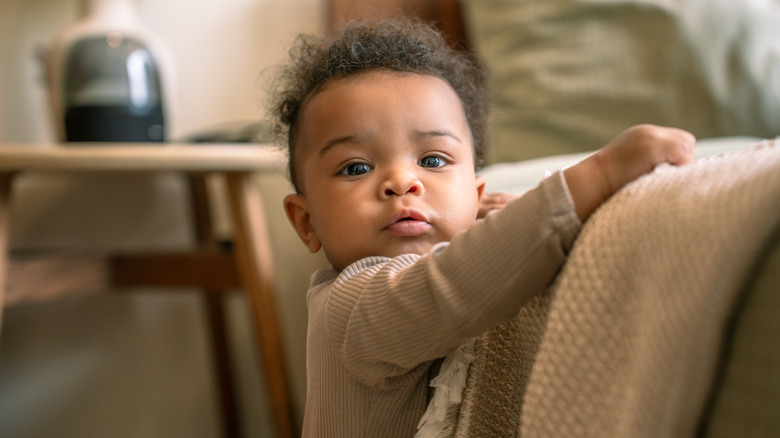 Un bébé tenant une couverture et regardant directement la caméra