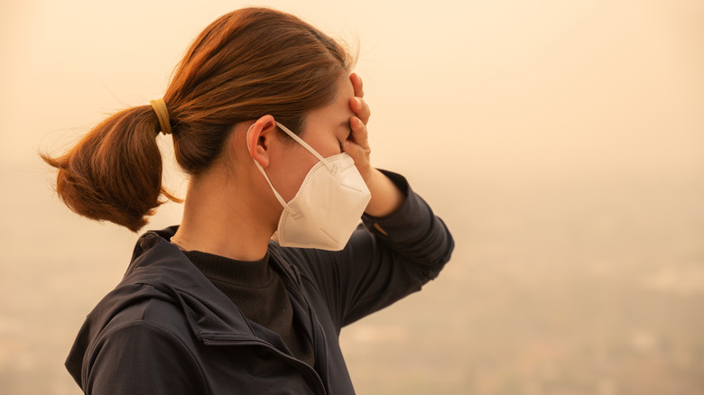 Une femme portant un masque et se tenant la tête alors que la fumée d'un feu de forêt cache la ville en arrière-plan