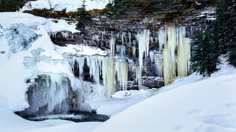 Cascades gelées avec de longs glaçons suspendus aux rochers jusqu'au sol recouvert de neige.