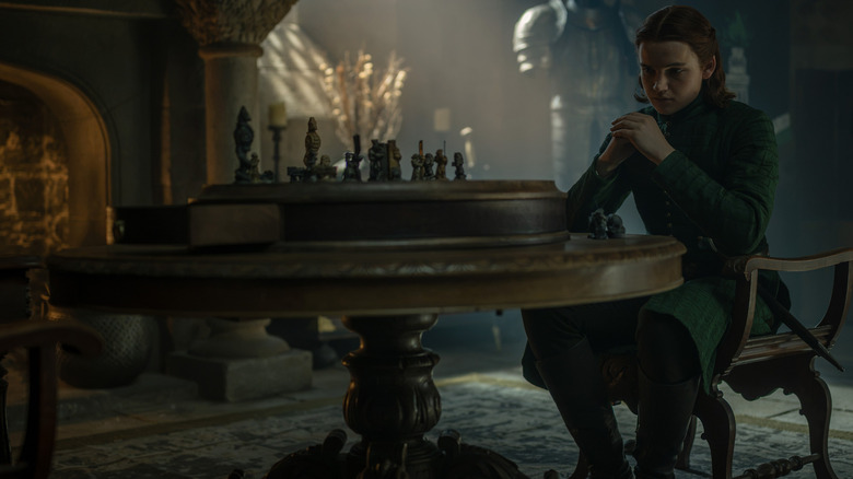 Benjamin Evan Ainsworth dans le rôle de Daeron Targaryen assis à une table avec des figurines dessus dans La Maison du Dragon
