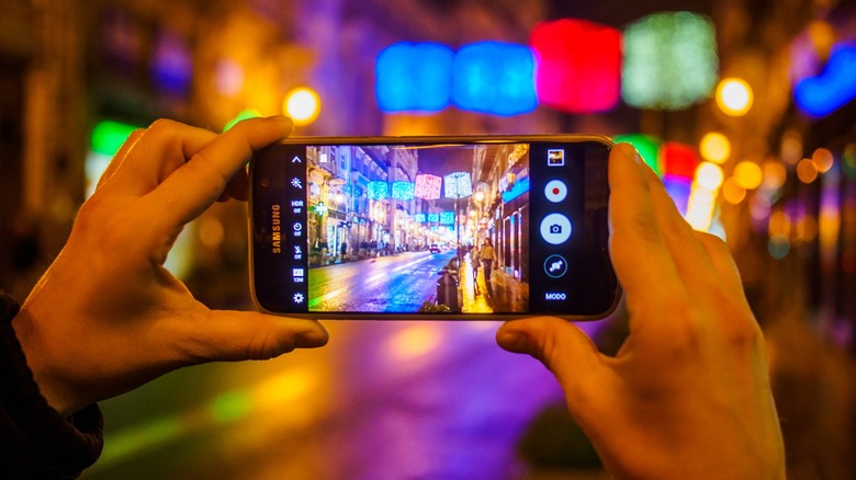 Une personne prenant une photo d’une rue de ville la nuit à l’aide d’un téléphone Samsung.
