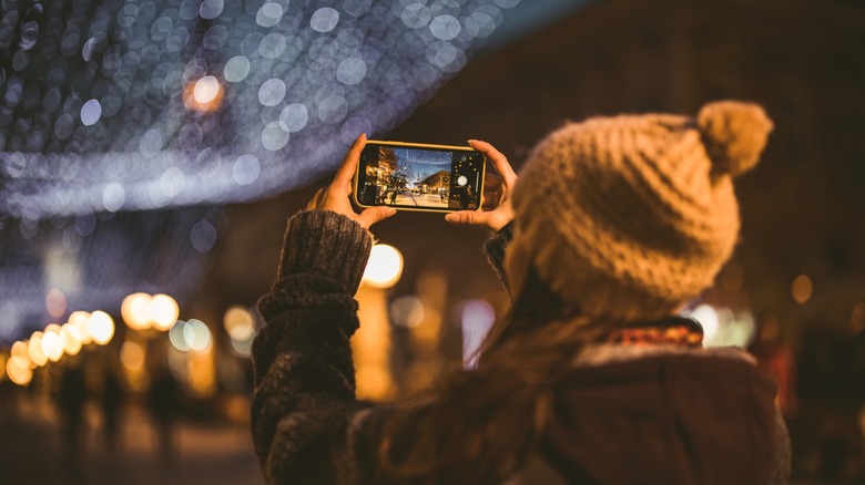 Une personne prenant une photo d’une scène de rue en soirée sur son smartphone.