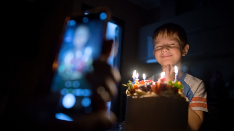 Un téléphone prend en photo un jeune enfant illuminé par des bougies sur un gâteau.