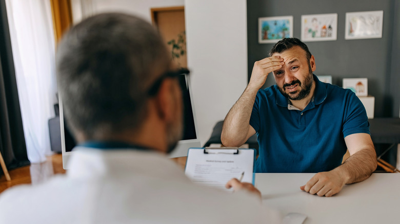 Homme avec la main sur la tête décrivant les symptômes à un médecin
