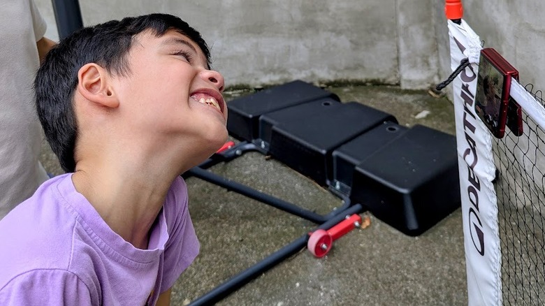 Un enfant souriant devant l'appareil photo d'un téléphone suspendu à un filet de pickleball