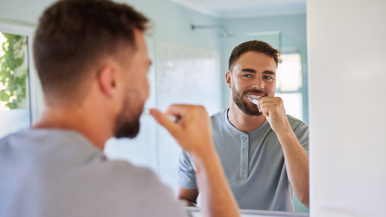 Homme se brossant les dents en regardant dans le miroir de la salle de bain