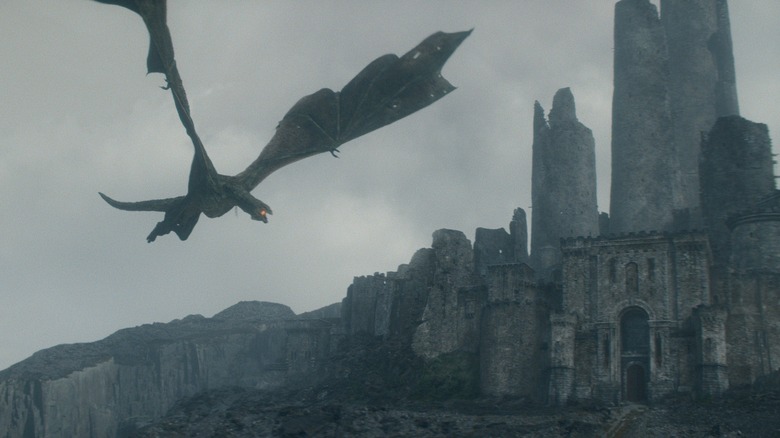 Un énorme dragon survolant les ruines d'un vieux château et se préparant à cracher du feu dans la Maison du Dragon