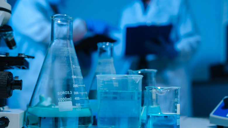 Un gros plan de plusieurs flacons avec des scientifiques conversant sur un arrière-plan flou.