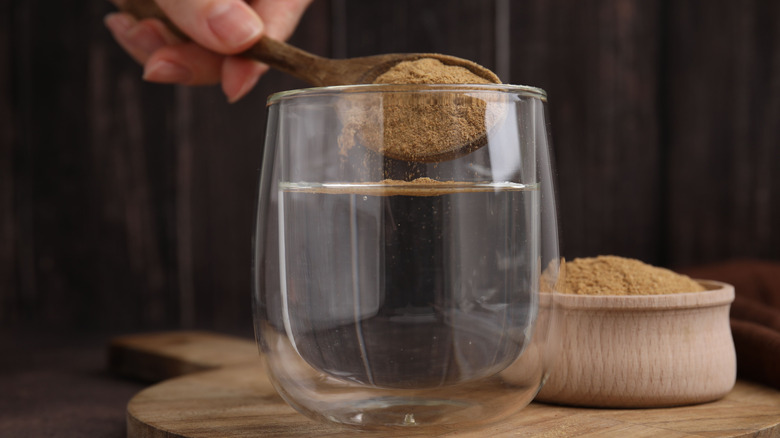 Main ajoutant une cuillerée de cosse de psyllium au verre d'eau
