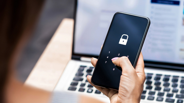 Une femme assise devant un ordinateur portable tenant un téléphone avec un écran de code d'accès dessus