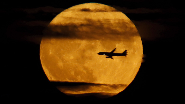 Vol d'avion et nuages ​​légers sillonnant devant une lune d'esturgeon jaune orangé