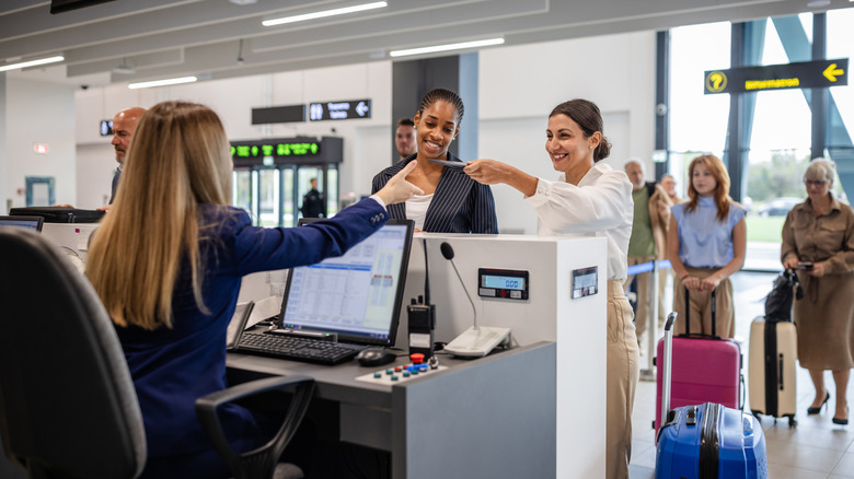 Deux femmes remettent leurs documents de voyage à un membre du personnel d'enregistrement au comptoir de l'aéroport.