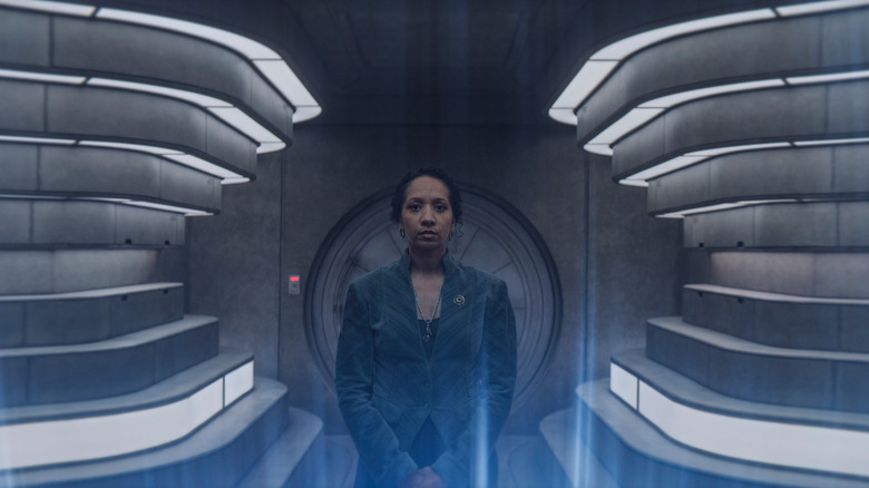 Alexandria Riley dans le rôle de Camille Sims debout dans une pièce bien éclairée en face d'un affichage de lumières bleues à Silo