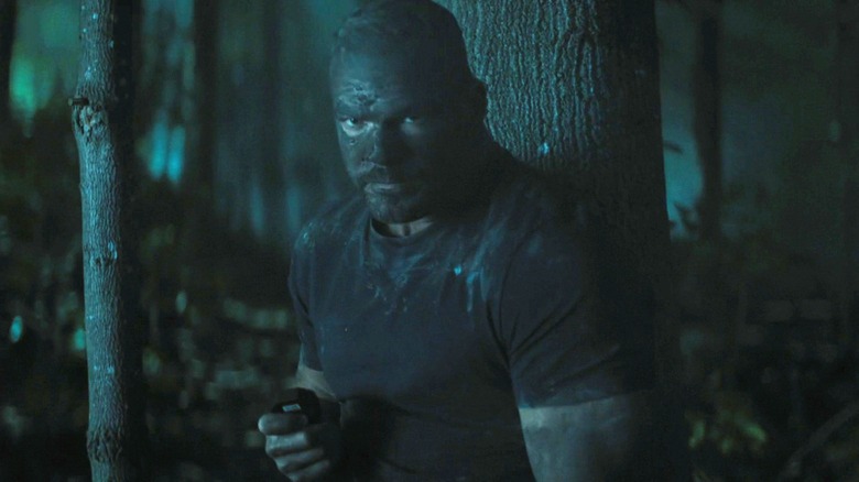 Jack Reacher d'Alan Ritchson se tient la nuit dans une forêt couverte de boue dans Reacher