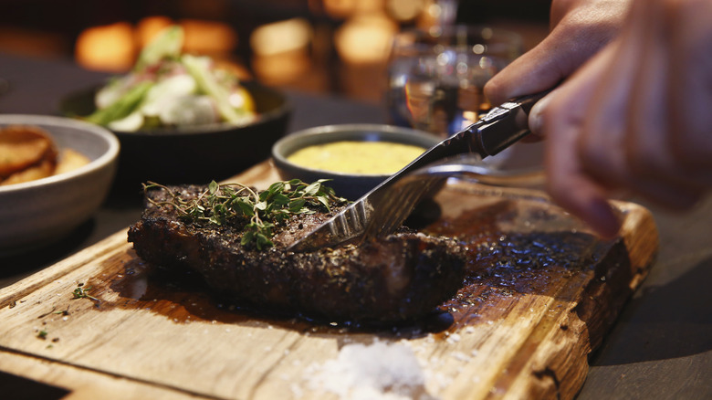 Mains coupant un steak sur une planche