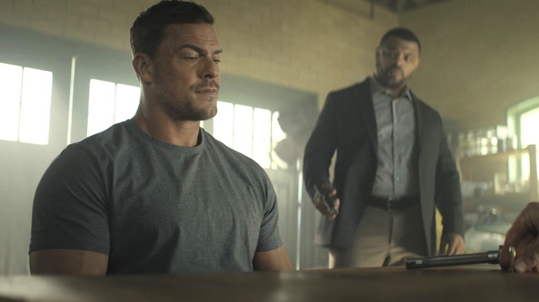 Jack Reacher d'Alan Ritchson regarde un pistolet sur une table dans Reacher