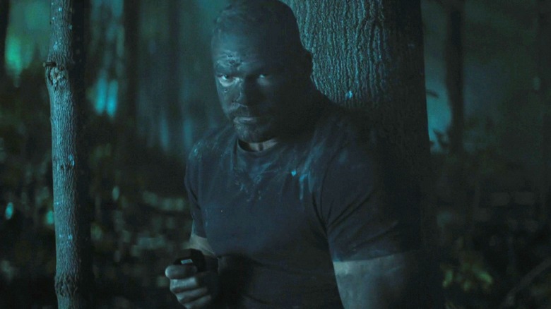 Jack Reacher d'Alan Ritchson se tient la nuit dans une forêt couverte de boue dans Reacher