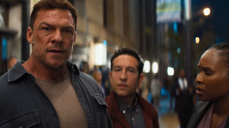 Alan Ritchson dans le rôle de Jack Reacher debout dans une rue animée à côté de Chris Marquette dans le rôle de Jacob Merrick et Sydelle Noel dans le rôle de Tamara Green dans Reacher