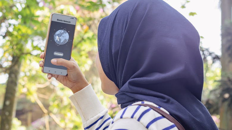 Une femme au foulard bleu se connecte au fournisseur de réseau sur un smartphone à l'extérieur