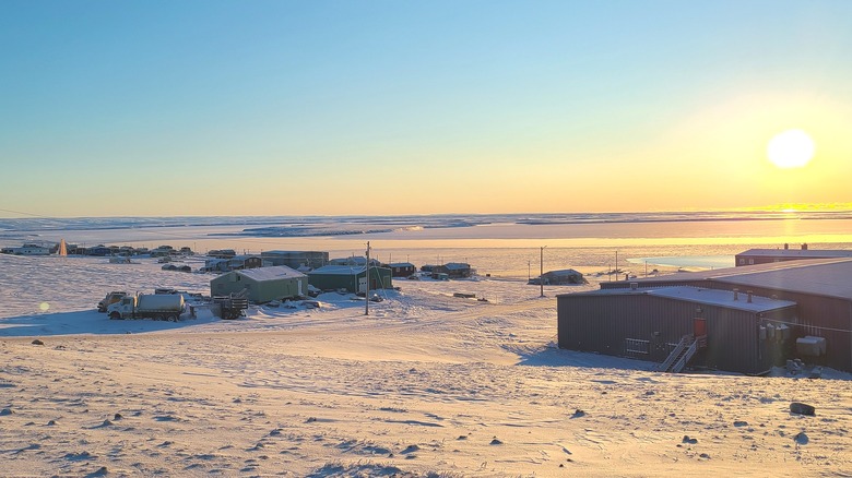 Communauté enneigée de Sachs Harbour sur l'île Banks avec le soleil se levant au loin