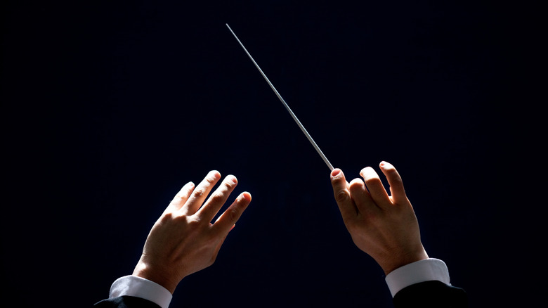 Un gros plan des mains d'un chef d'orchestre tenant un bâton en l'air.