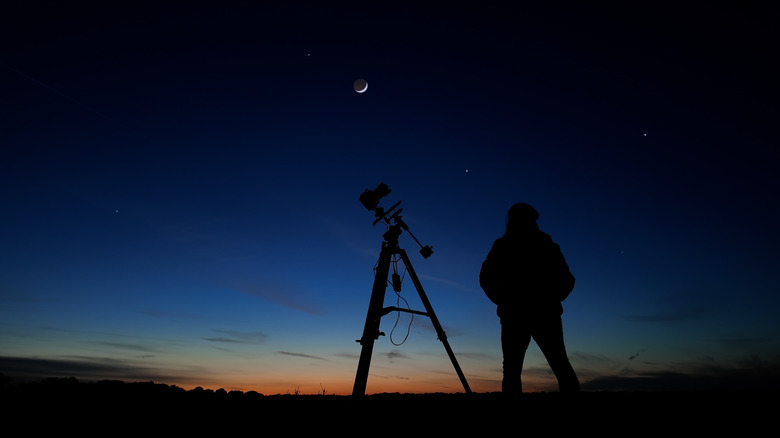 une personne debout avec un télescope pour observer les étoiles