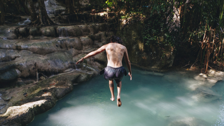 Homme blanc sautant dans la piscine de la jungle, les vignes et les rochers environnants