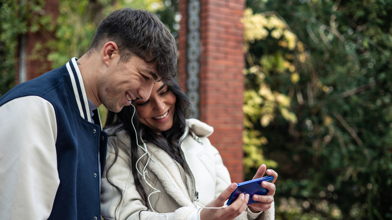 Un couple portant des écouteurs et riant devant l’écran d’un smartphone