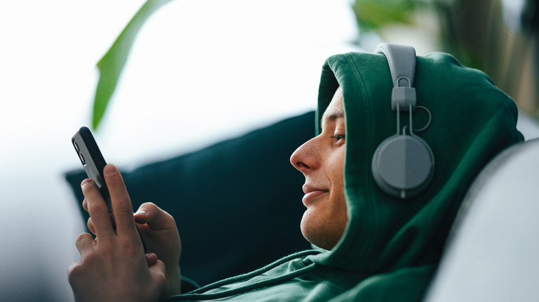 Un jeune homme portant des écouteurs et tapant sur son smartphone