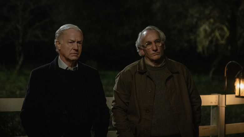 Reed Birney dans le rôle de Henry debout, les mains dans les poches, près d'une clôture à côté de Matt Craven dans le rôle de Victor Crnkovich dans Silo
