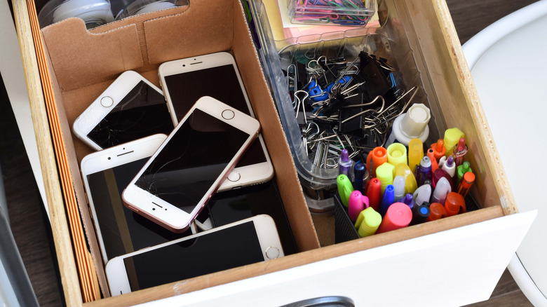 Une boîte de vieux iPhones cassés dans un tiroir à déchets.