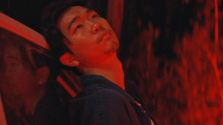 James s'appuie contre l'arrière d'une Jeep et regarde le ciel nocturne alors qu'il est baigné de lumière rouge dans It Ends.