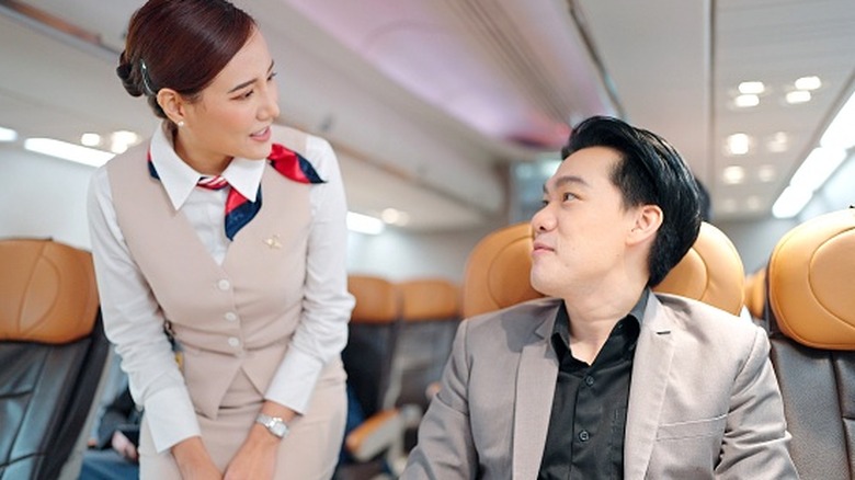 Une hôtesse de l'air discute avec un passager dans un avion.