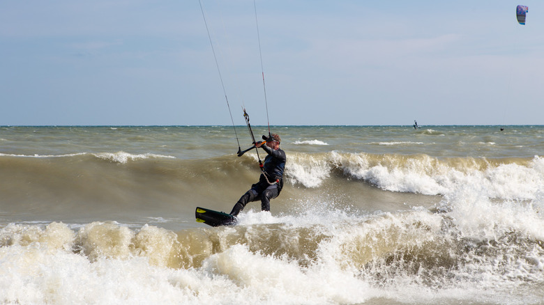 Un homme en combinaison s'accrochant à une barre de kitesurf tout en glissant sur les vagues.