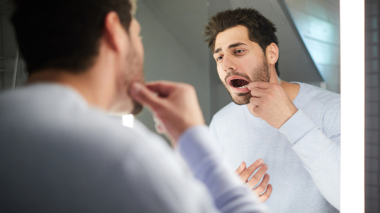 Homme regardant les dents dans un miroir de salle de bain