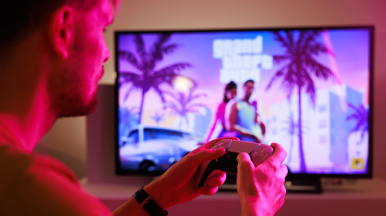 un homme avec une manette de Playstation regarde le logo de Grand Theft Auto 6 à la télévision