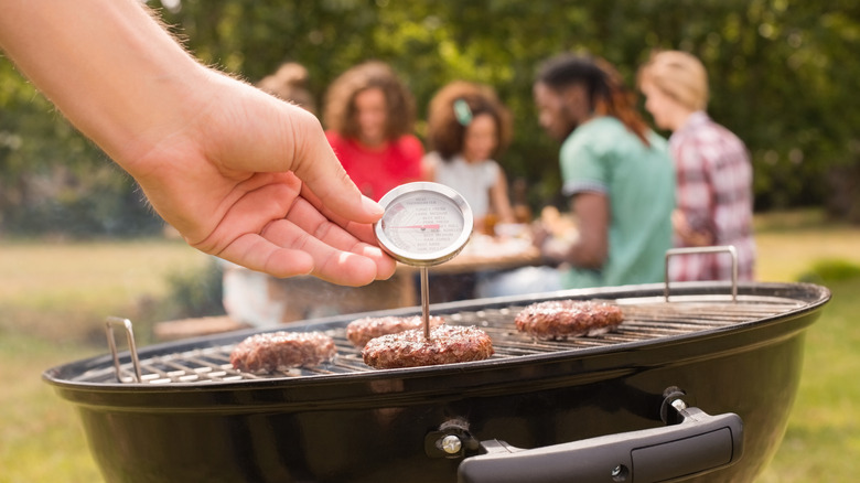 Personne vérifiant les hamburgers sur le grill avec un thermomètre à viande