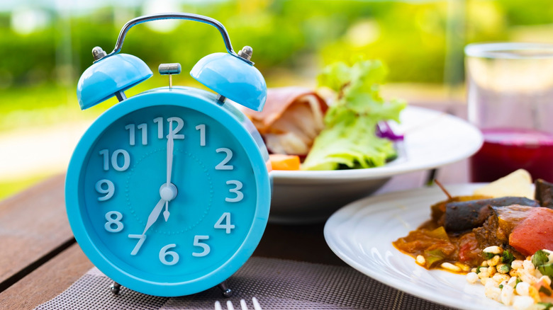 Un réveil bleu posé à côté d’une assiette de nourriture et devant un saladier