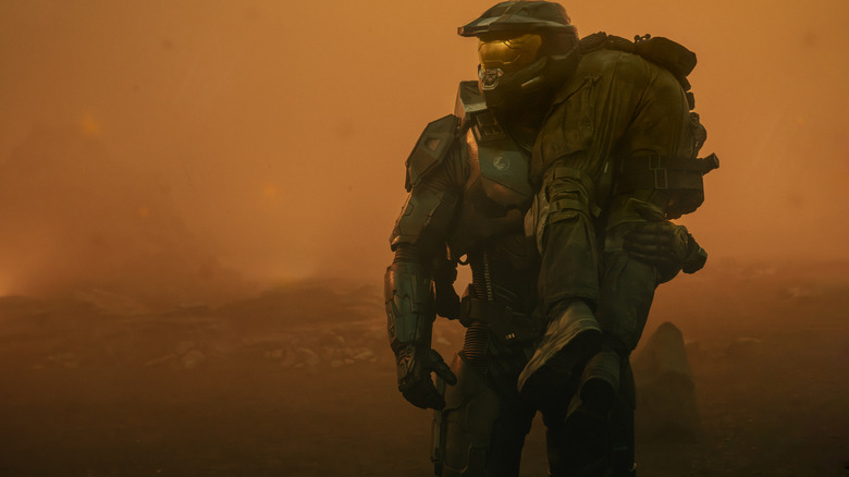 Pablo Schreiber en tant que Master Chief debout sur un monde extraterrestre couvert de brouillard et portant un soldat tombé sur son épaule dans Halo