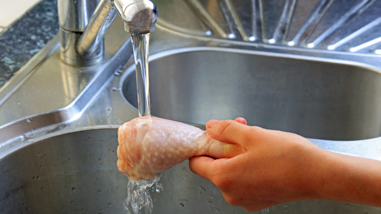 Personne lavant une cuisse de poulet sous le robinet