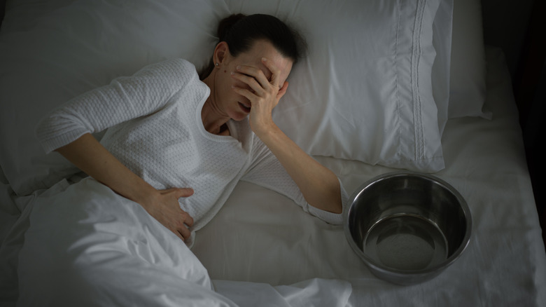 Femme couchée dans son lit souffrant de nausées avec un bol vide à côté d'elle