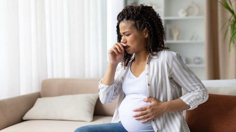 Femme enceinte luttant contre les nausées en étant assise sur un canapé