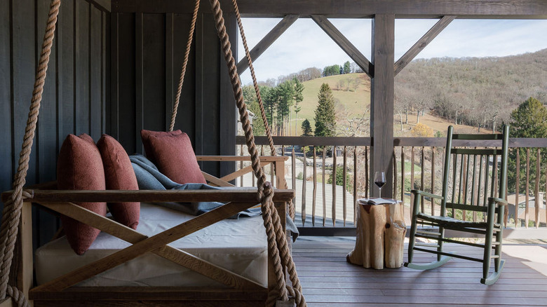 Un banc pivotant rembourré sur une terrasse avec un fauteuil à bascule donnant sur le parc depuis une suite du Silverbell Lodge de Cataloochee Ranch à Maggie Valley, en Caroline du Nord.