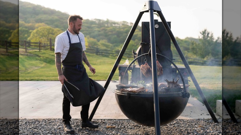 Un chef tenant des pinces et regardant un fumeur extérieur à l'extérieur du restaurant Switchback du Cataloochee Ranch à Maggie Valley, en Caroline du Nord.