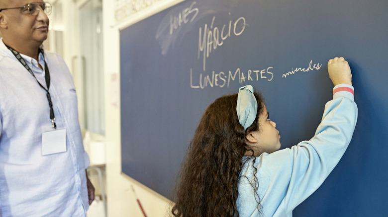Jeune fille écrivant sur un tableau noir tandis qu'un instructeur masculin regarde