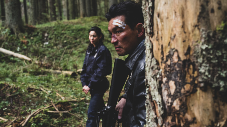 Hwang Jung-min dans le rôle de Bum-seok debout dans une forêt avec un bandage sur la tête à côté de Hoyeon dans le rôle de Sung-ae dans Hope