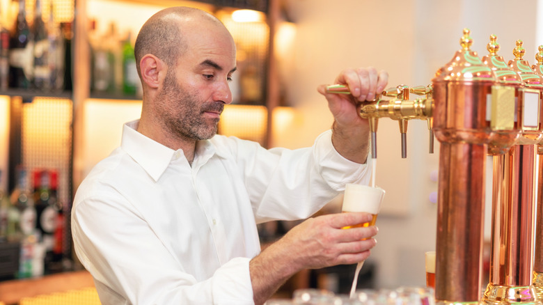 Un barman verse de la bière alors qu'il se tient au comptoir du bar.